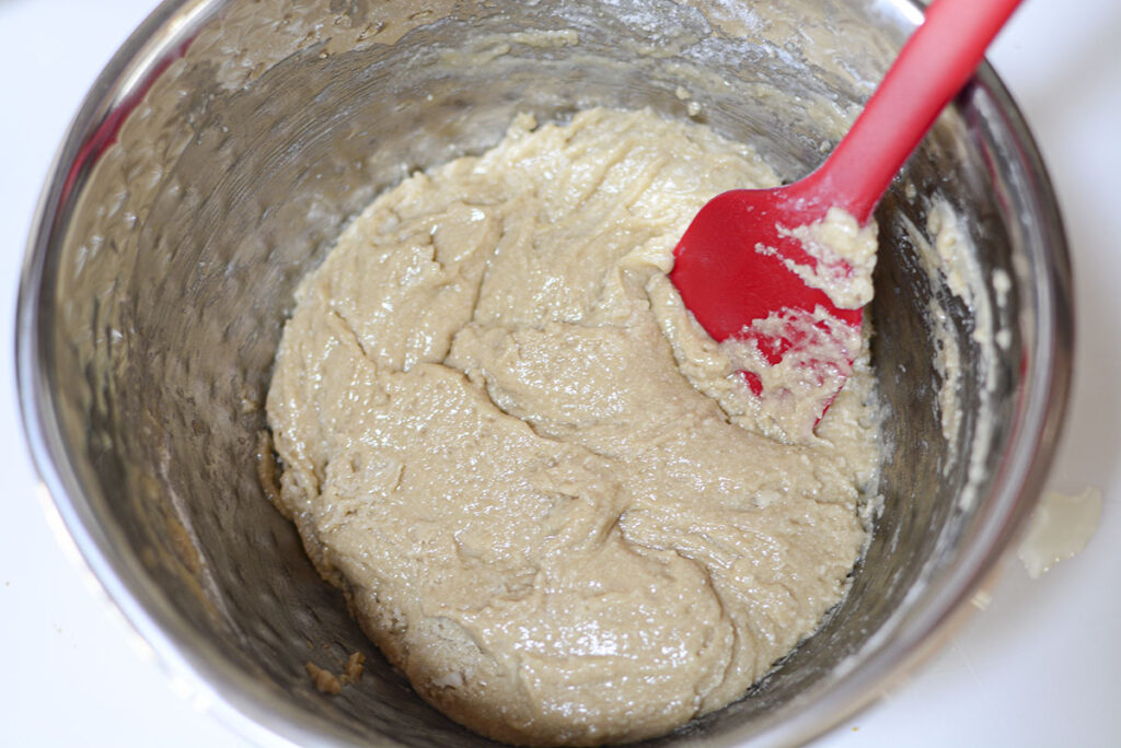The cookie batter in a silver bowl with a red spatula.
