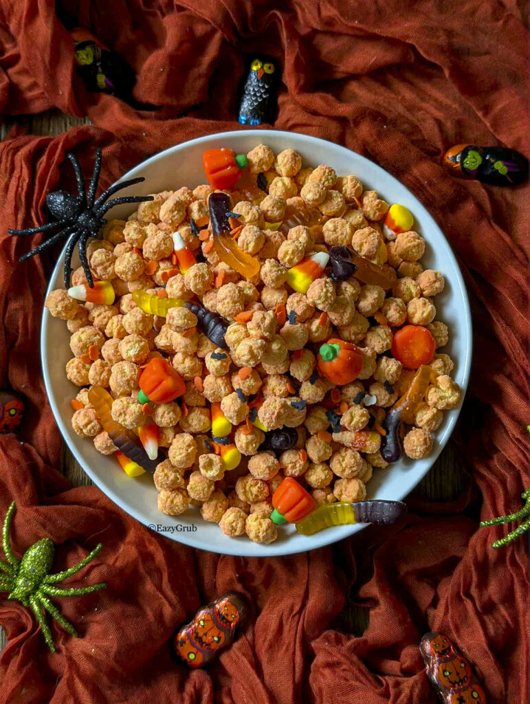 A bowl of Halloween snack mix surrounded by festive orange cloth and decorative spiders.