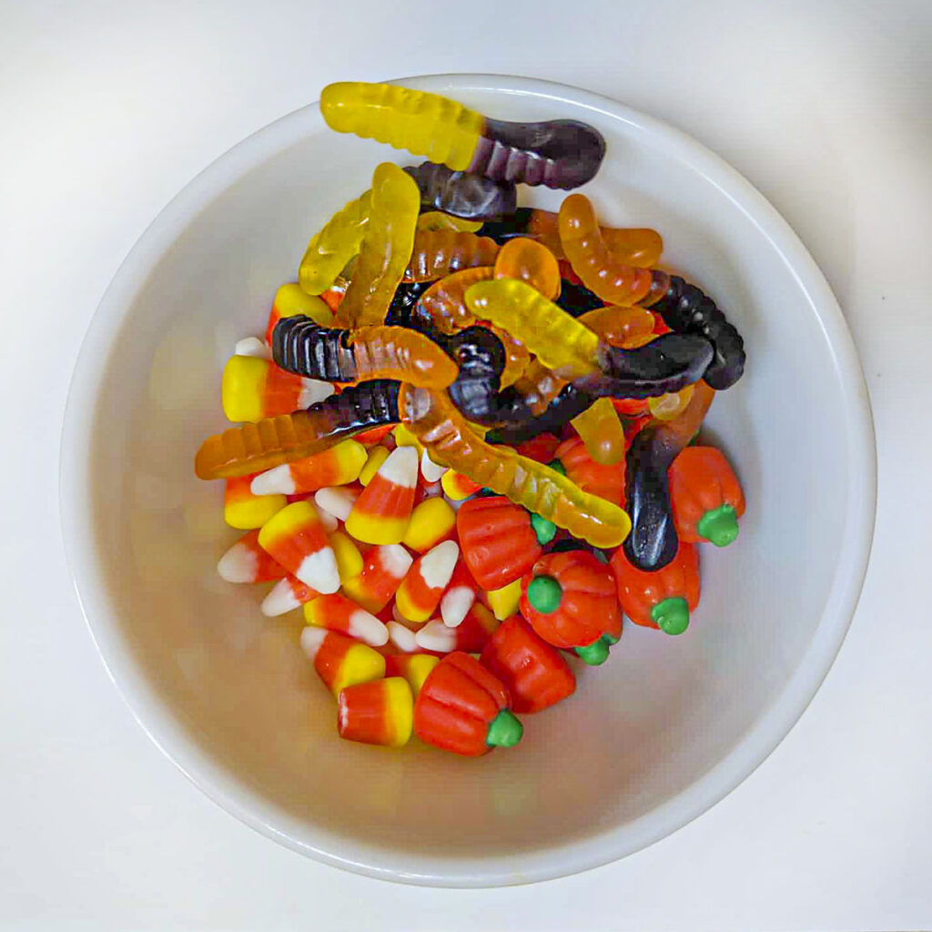 White bowl filled with gummy worms, candy corn, and pumpkin-shaped candies