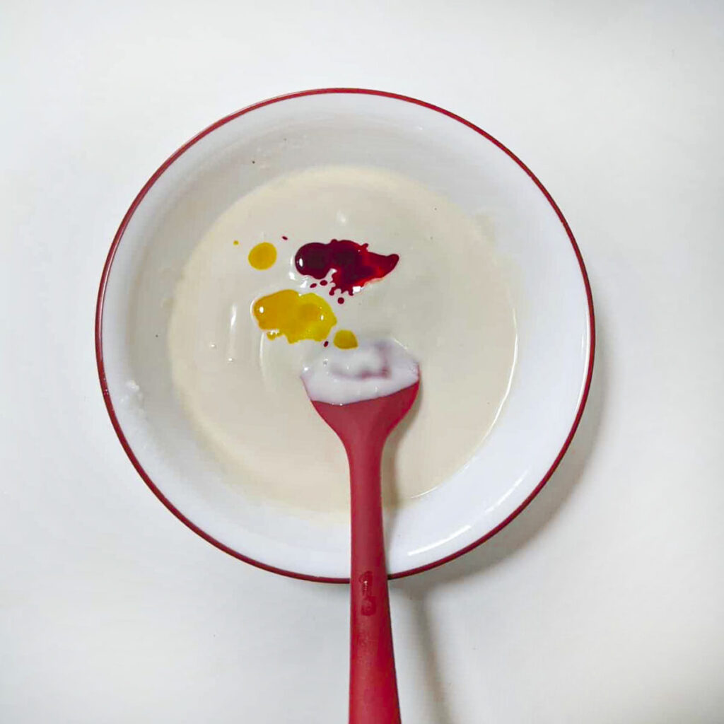 Drops of red and yellow food coloring added to a bowl of melted white chocolate