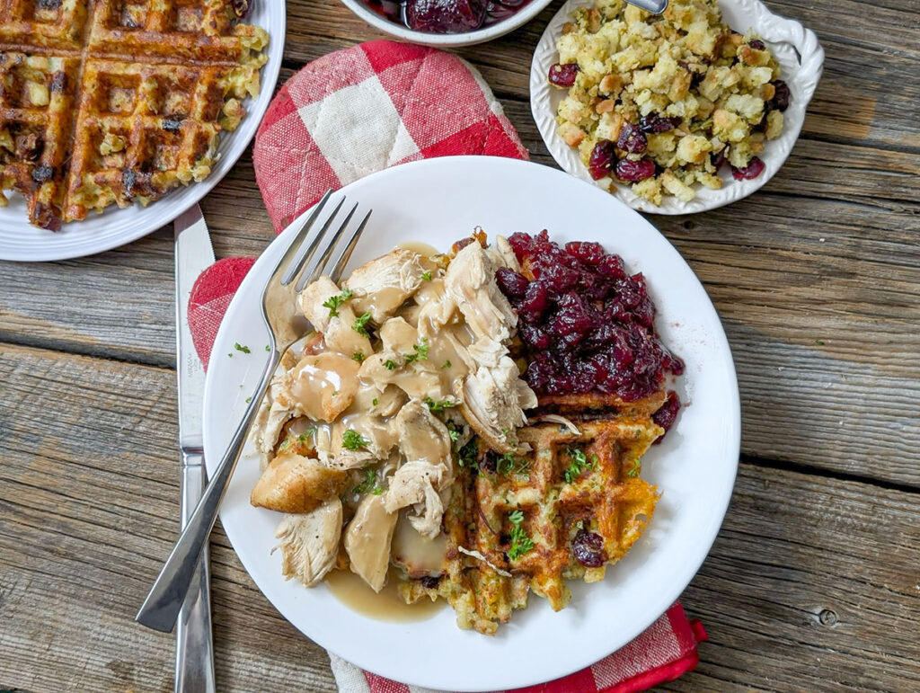 Dinner plate set with a savoury waffle, sliced poultry with gravy, and berry sauce next to side dishes