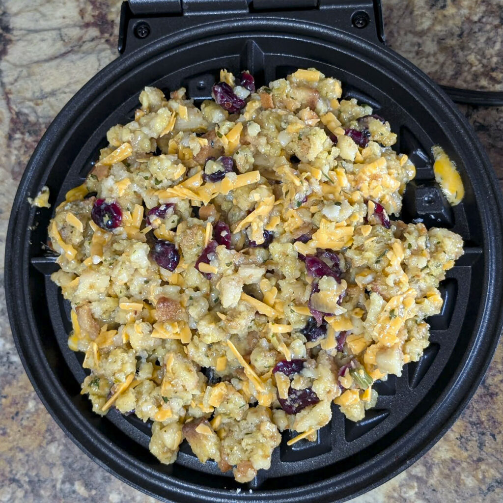 Uncooked stuffing and cheese mixture spread onto a heated waffle iron grid