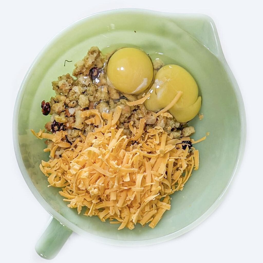 Green mixing bowl filled with raw eggs, shredded cheese, and stuffing mix before combining